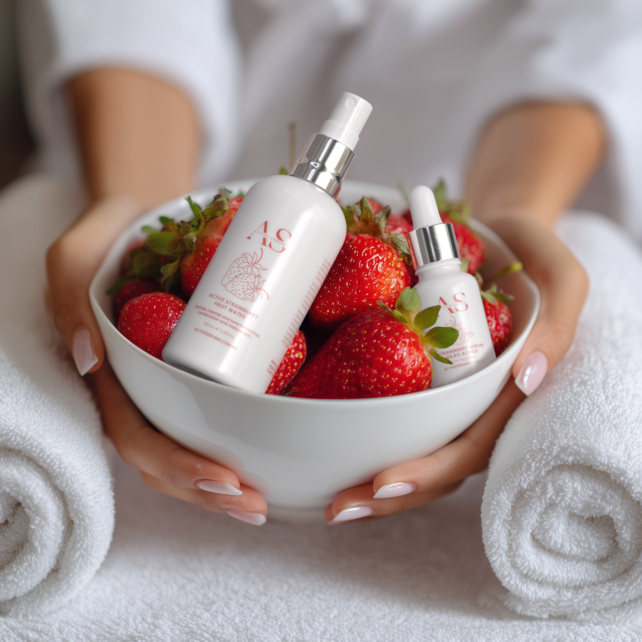 Active Strawberry Duo skincare bottles in a bowl of fresh strawberries, held by a person at a beauty spa.