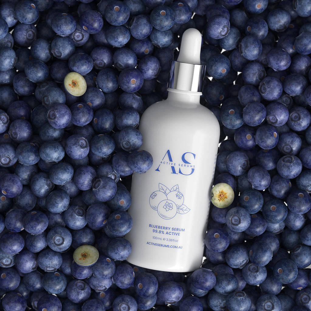 Active Serums 100ml Blueberry Serum bottle nestled in a flatlay of fresh, whole blueberries.